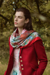 SCAPA AW25 Woman in a red coat and floral dress standing in a grassy field with trees.